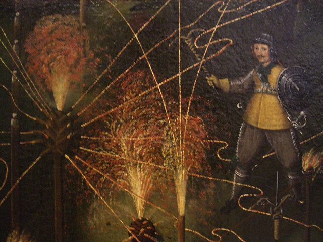 Figure 3 — A painted detail of a pyrotechnic performance: a man in a slashed doublet and helmet stands amid fountains of golden fire, holding a fire-club in one hand and carrying a spinning wheel of fire on h…