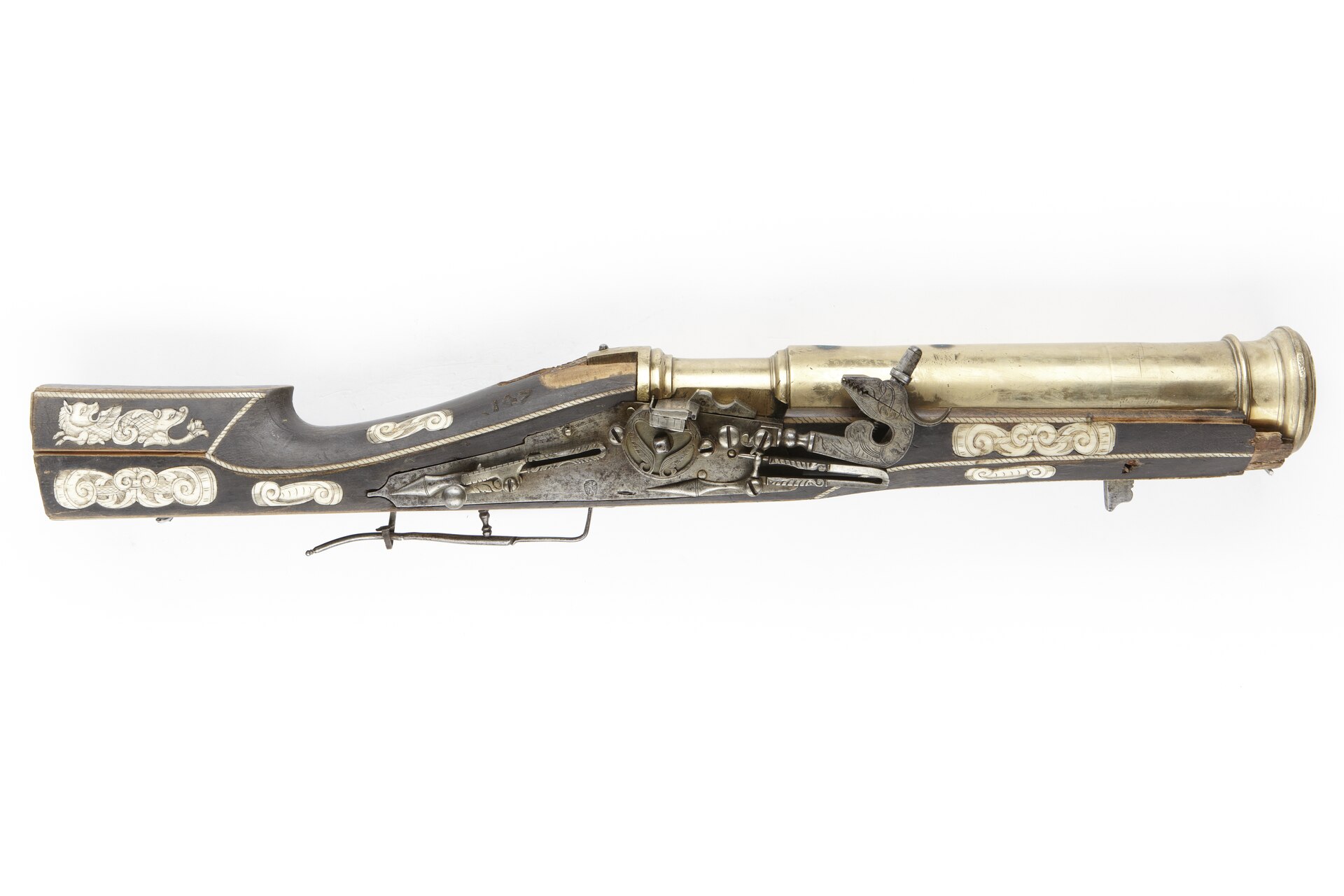 Figure 3 — A wheellock grenade gun of about 1600 with an unusually long brass barrel, the stock inlaid in bone with scrollwork and a griffin. The cup is at the far end of a barrel long enough to belong on a s…