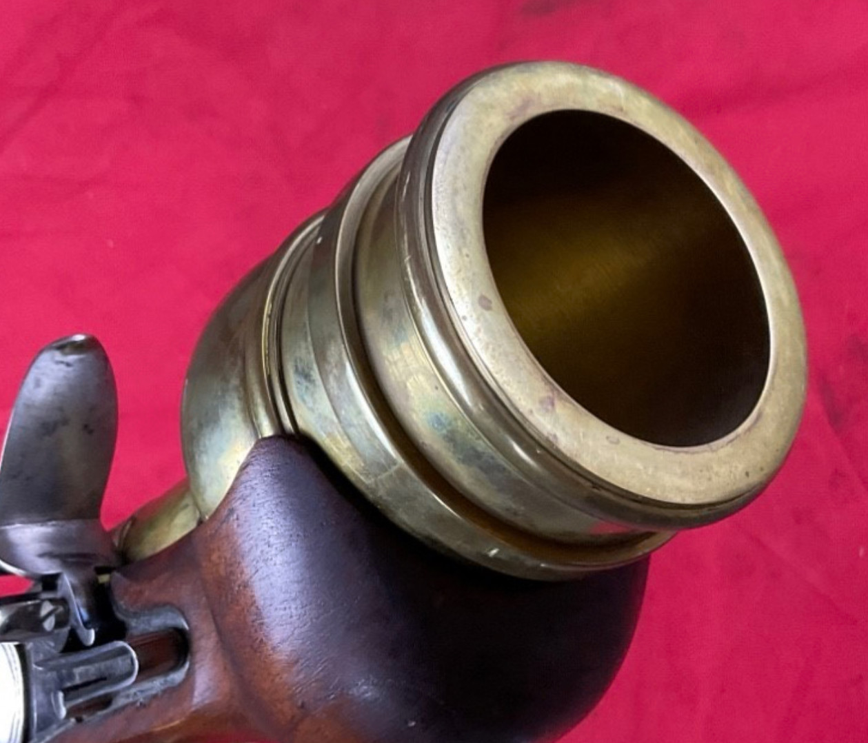 Figure 2 — The muzzle of a Veteran Arms hand mortar in close-up: a heavy, stepped, polished brass cup, its bore clean and bright, mounted on a dark walnut stock, with the flintlock just visible at the lower e…