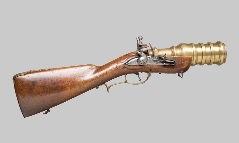 Figure 2 — A German flintlock hand mortar in profile: a plain full stock, a small lock, and a heavy stepped brass barrel with three broad reinforcing rings toward the muzzle. Source: via peashooter85.