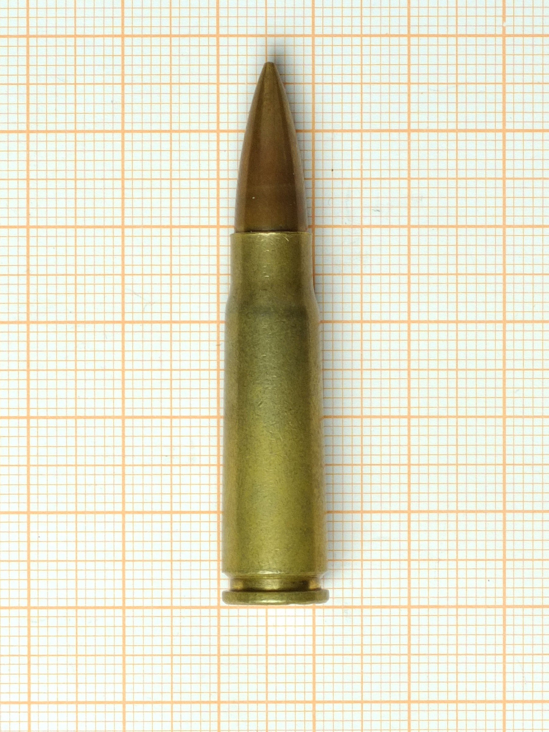 Figure 1 — A brass-cased 7.62×39 mm M43 cartridge photographed against graph paper. The round is short, fat and unglamorous, and it is the reason the rifle around it is the size and shape it is.