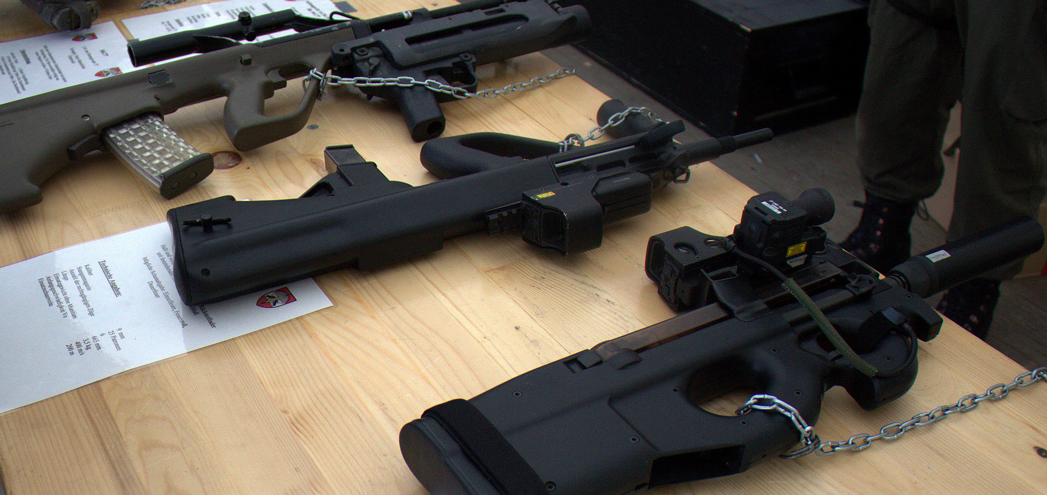 Figure 15 — P90s on display alongside other service weapons. Seen next to conventional arms, the compactness the bullpup layout buys is obvious — and so is how much of the weapon is magazine.