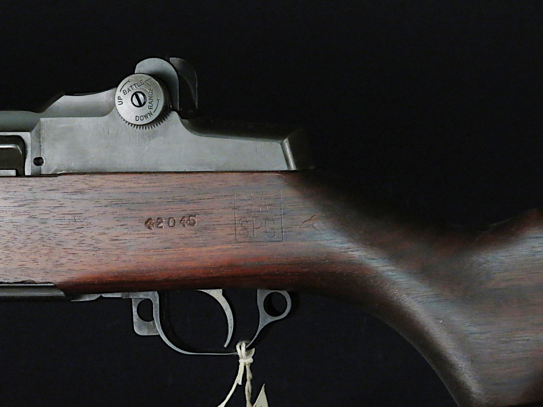 Figure 2 — A Springfield "SA / SPG" cartouche on the left side of an M1 stock in the Smithsonian's collection, beside the stamped number 42045. A stock like this one records who accepted it and roughly when. …