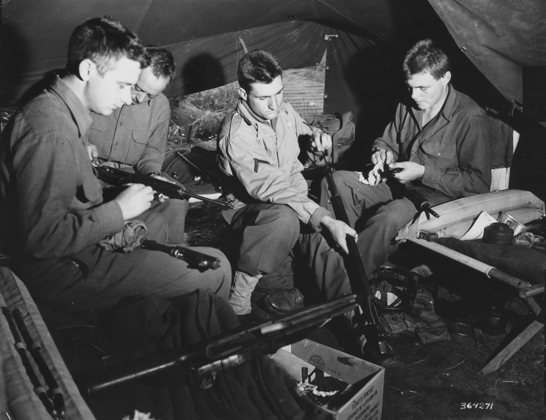 Figure 2 — Four infantrymen cleaning their rifles on June 1, 1944, "awaiting orders for the big push against the European continent." — Photograph: U.S. Army Signal Corps (photographer Schillinger), public do…