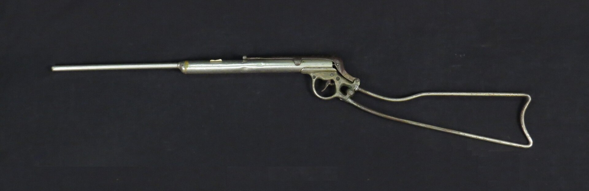 Figure 2 — An early all-metal Daisy with the wire skeleton stock that defines the first generation: the entire buttstock is one length of heavy wire bent to a butt shape and anchored at the trigger group. It …