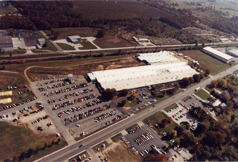 Figure 2 — Aerial view of the Daisy plant at Rogers, Arkansas: a single long span under one roof, set beside a rail line with a parking lot to match. The photograph is well after the 1958 move, but the site p…