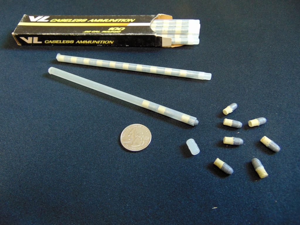 Figure 3 — An original V/L packaging set: the printed carton, two ten-round plastic tubes, loose rounds and a coin for scale. On a caseless cartridge the tube is not packaging in the ordinary sense - it is ta…
