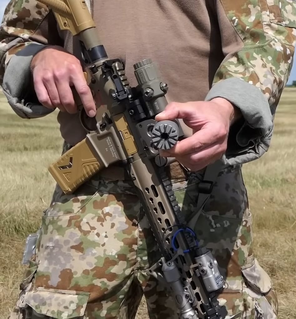 Figure 4 — A short-barrelled 5.56 carbine wearing a compact suppressor. Short barrel plus fast firing schedule is exactly the combination that makes the material rating stop being marketing. Source: commons.w…